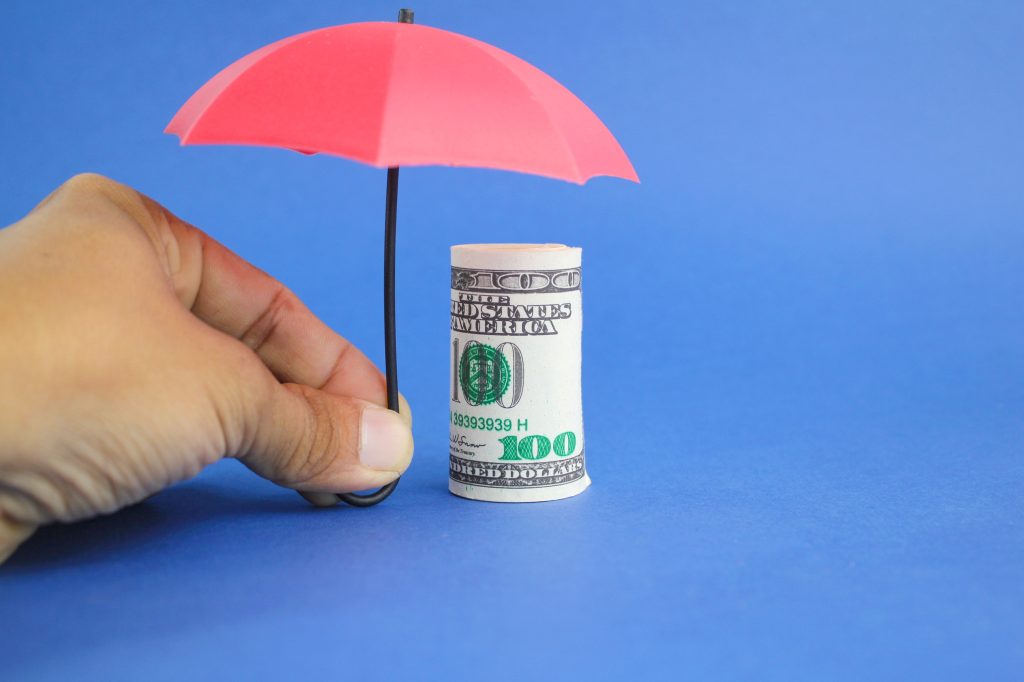Rolled dollars covered by pink umbrella on a blue background.