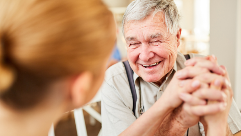Old man smiling holding hands with caregiver