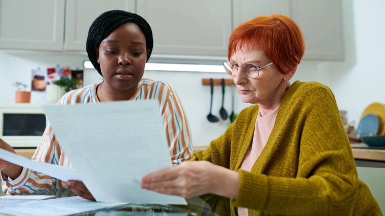 Private caregiver assisting elderly woman with paperwork.